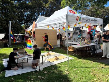 Outdoor community event with rainbow flags and creative activities under tents.