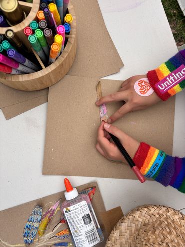 Child coloring cut-out shapes on brown paper with markers and glue nearby.