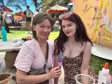 Two young women enjoying an outdoor event with art and crafts.