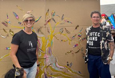 Two people stand smiling in front of a colorful tree art installation.