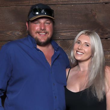 Smiling couple posing against a wooden wall, dressed casually.