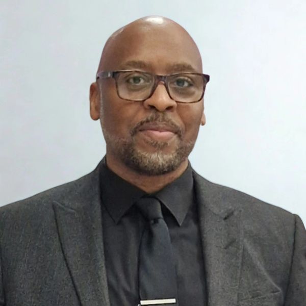 Man in a dark suit and glasses smiling gently.