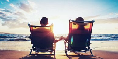Couple holding hands on beach chairs at sunset by the ocean.