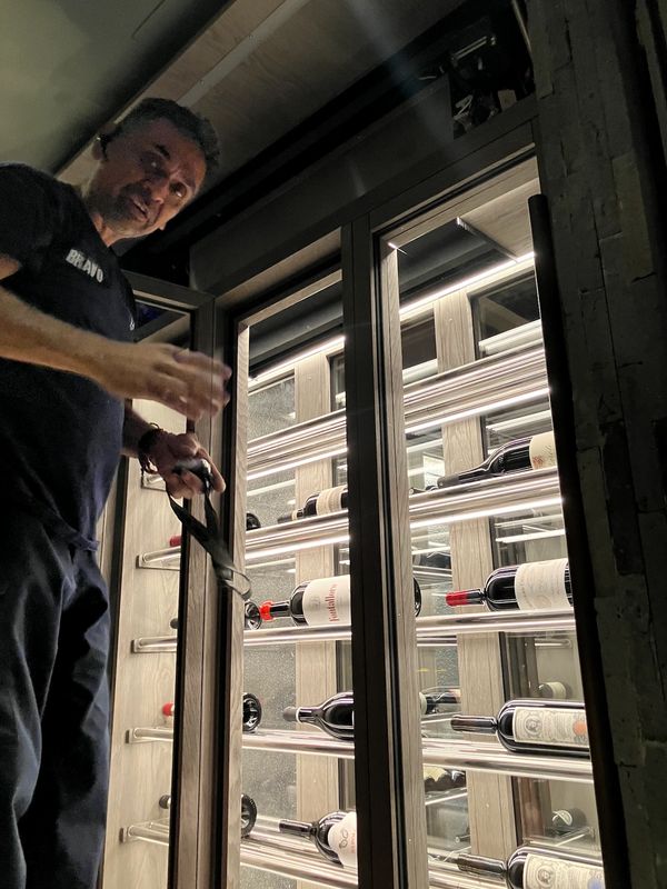 A man opening a wine fridge in dim lighting.