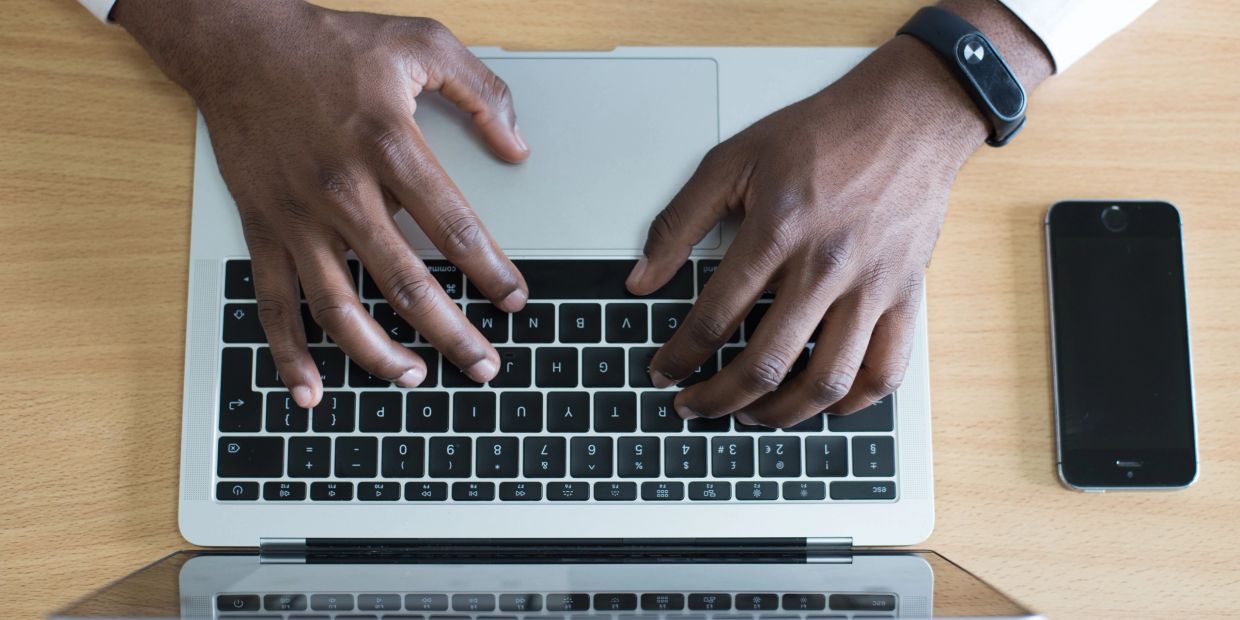 Hands typing on a laptop keyboard with a phone nearby.