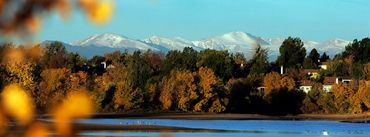 Autumn trees by a lake with snow-covered mountains in the background.
