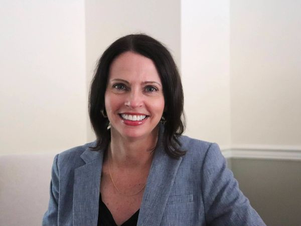 A woman in a gray blazer smiling indoors.