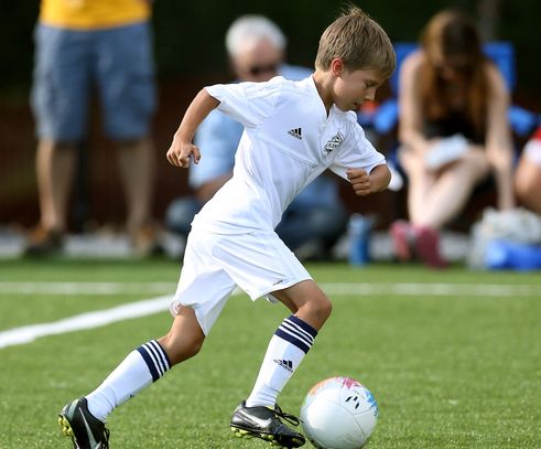 Young boy playing soccer, dribbling the ball on a green field.