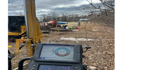 Construction site with a monitoring device in the foreground and workers in the background.