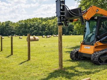 A machine installs wooden fence posts in a green field.