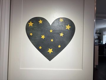 Black heart with yellow stars painted on a white door.
