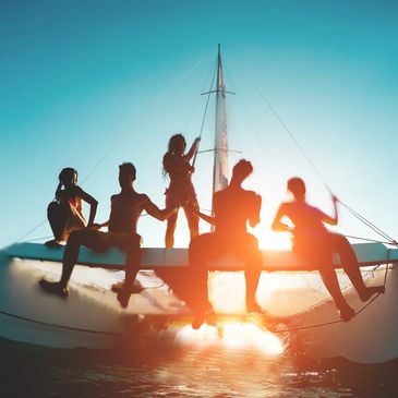 Silhouettes of five people enjoying a sunset on a catamaran sailboat.