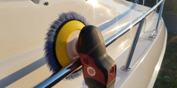 Polishing a boat's exterior with a power buffer in sunlight.