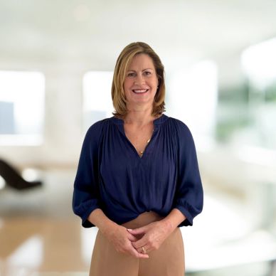 Smiling woman in a navy blouse and beige pants standing indoors.