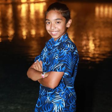 Smiling boy with crossed arms wearing a blue patterned shirt at night.