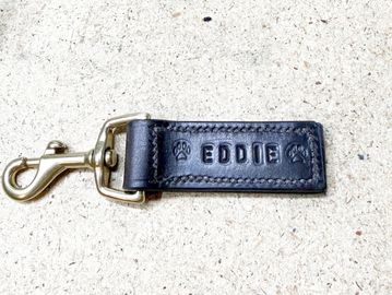 Leather keychain with the name 'Eddie' and paw prints on a light surface.
