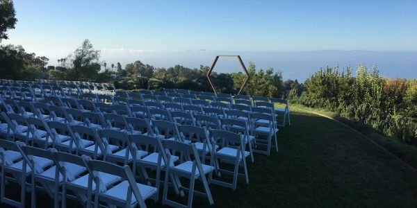 Empty white chairs arranged outdoors for an event with ocean view.
