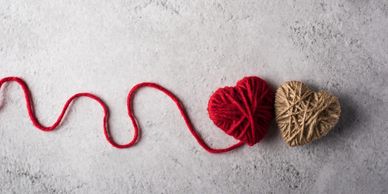Two heart shapes wrapped in yarn, connected by a red string.