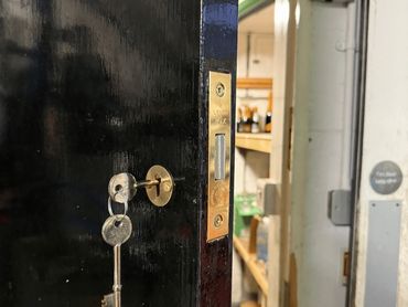 Keys inserted in a black door lock with a glimpse of a storage room behind.