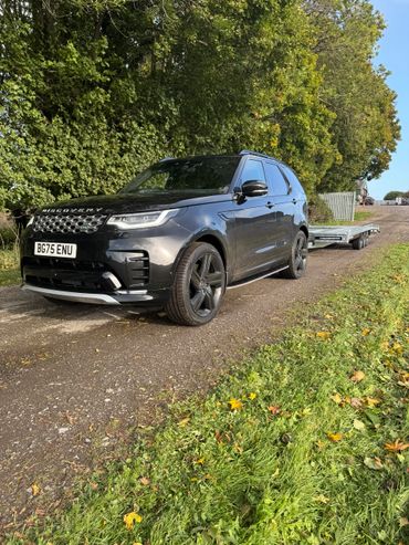 Black Land Rover Discovery towing a trailer on a rural dirt road.