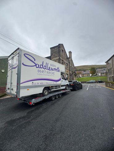Delivery truck for Saddleworth Beds being transported on a trailer in a village.