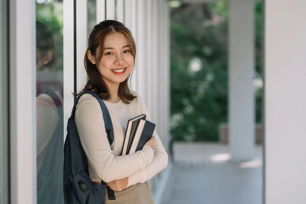 Female high school student holding books and smiling, happy about SAT score. Walker Test Prep Review