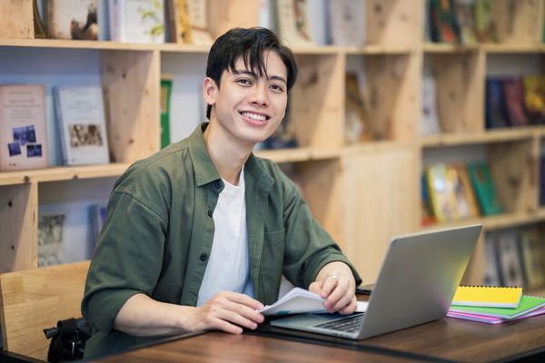 Happy dark-haired student in library smiling and studying to increase SAT score. Walker Prep Review.