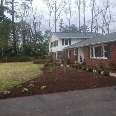 A suburban house with newly mulched garden beds and sparse young plants.