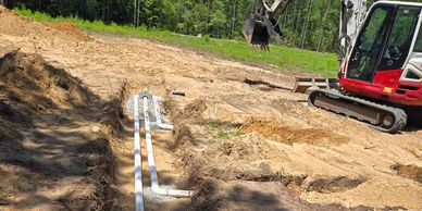 Excavator working on a trench with plumbing pipes laid out in a construction site.
