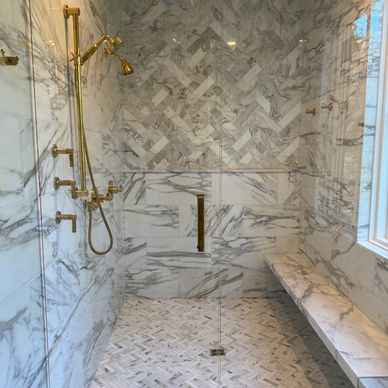 Luxurious marble shower with gold fixtures and a built-in bench.