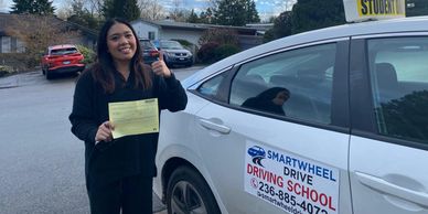 Young woman holding a certificate by a driving school car.
