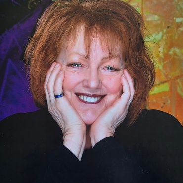 Smiling woman with red hair resting her face on her hands.