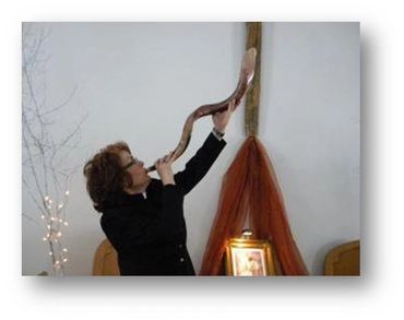 Person blowing a shofar in a decorated indoor setting.