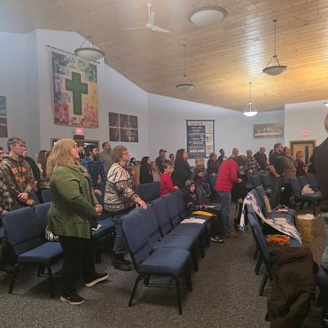 A group of people standing in a church with blue chairs and religious banners.