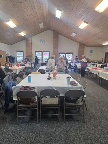 Community gathering in a wooden-ceiling hall with tables and chairs.