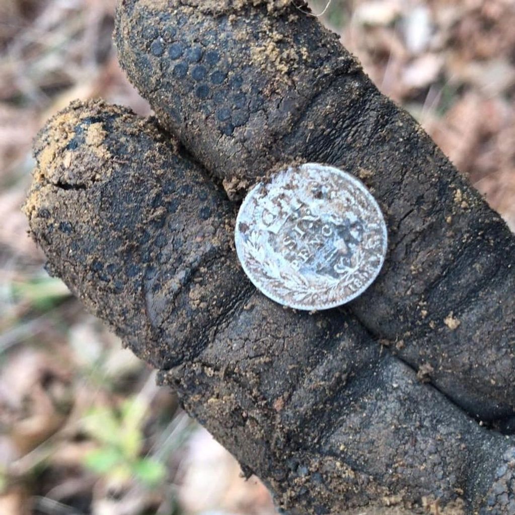 A dirty gloved hand holding a small, weathered coin.