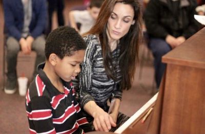 A woman teaching a boy to play the piano.