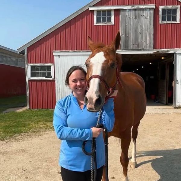 Smiling woman with a brown horse in front of a red barn.