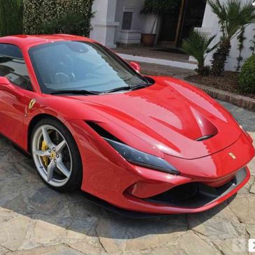 Shiny red Ferrari sports car parked on a stone driveway.