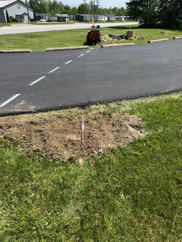 A machine is digging a trench across a paved road in a suburban area.