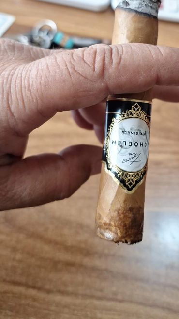 A hand holding a partially smoked cigar with a decorative band.