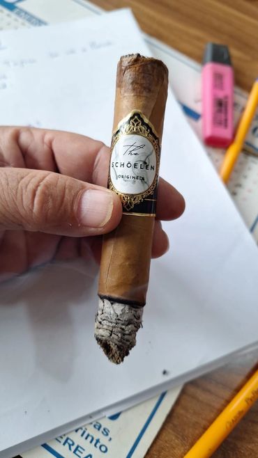 Hand holding a lit cigar with label The Schoellen Original.