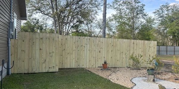 New wood privacy fence extends from the side of a house, then cuts back from driveway and continues