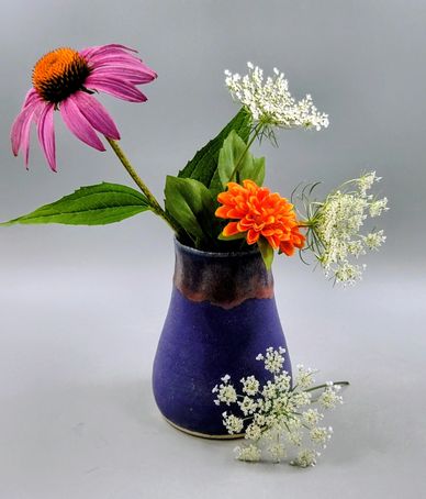 A small purple vase with a colorful flower arrangement.
