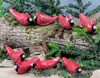 Red ceramic cardinals perched on a log with green pine branches.