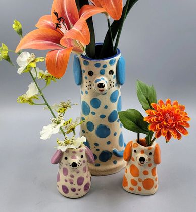 Three colorful dog-shaped vases with flowers inside them.