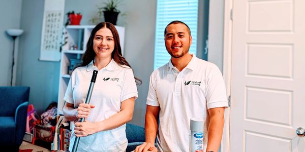 Two smiling cleaning professionals in white shirts holding cleaning supplies.