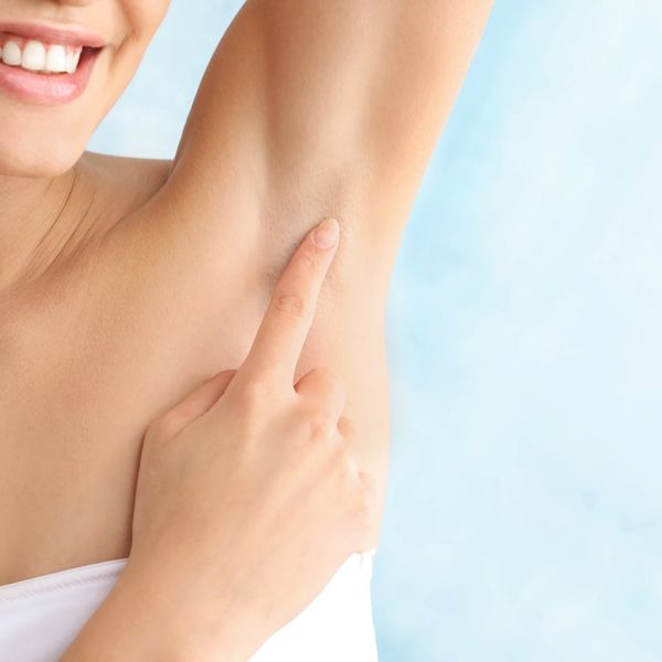 Woman holding up arm pointing to armpit that is hairless.