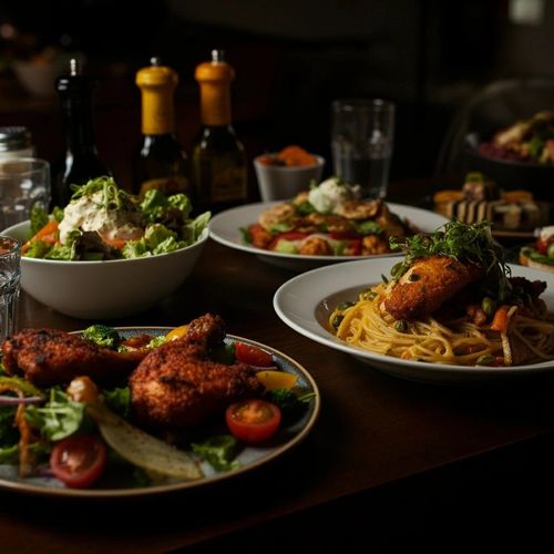 Set table with plates of chicken and pasta a bowl of salad and a glass of water.