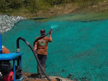 Worker spraying green hydroseeding mulch on a hillside for erosion control.